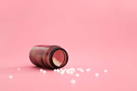 Close-up image of homeopathic globules in glass bottle on pastel pink background. Homeopathy pharmacy, herbal, natural medicine, alternative homeopathy medicine, healthcare. Free space, copy space.の写真素材
