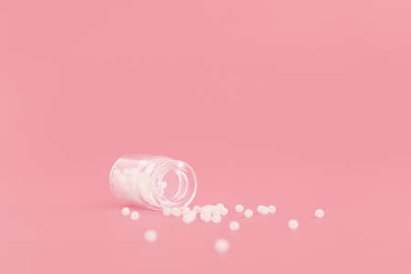 Close-up image of homeopathic globules in glass bottle on pastel pink background. Homeopathy pharmacy, herbal, natural medicine, alternative homeopathy medicine, healthcare. Free space, copy space.の写真素材