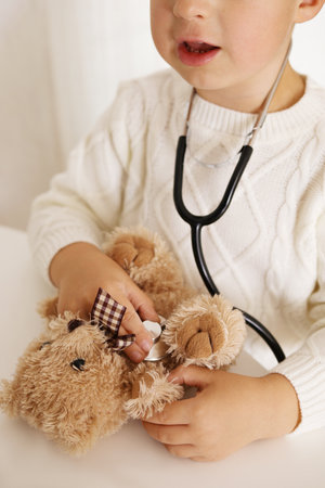 Cute little boy playing doctor at home and curing plush toy. Sweet toddler child using stethoscope. Having fun. Kids and medicine, healthcare.の写真素材