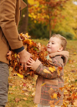 Outdoor fun in autumn. Father and son playing with autumn fallen leaves in park.の写真素材