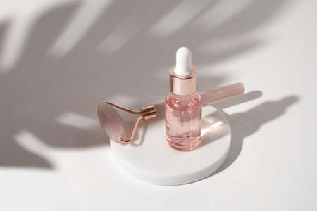 Massage quartz roller and pink glass bottle of cosmetic liquid transparent gel on white background. Dropper bottle, hyaluronic acid, oil, serum. Facial massage and relaxation. Gua Sha massage tools.の写真素材