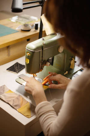 Closeup view of womans hands sewing fabric with a vintage, retro sewing machine. Fashion, creation and tailoring. Process of sewing in atelier or workshop.の写真素材