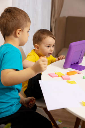 Happy kids with yellow and blue shirts doing arts and crafts together at their desk and watching...