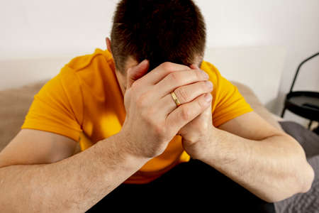 Depressed caucasian man with headache sitting alone on the bed. Stressed, lonely person, feeling...