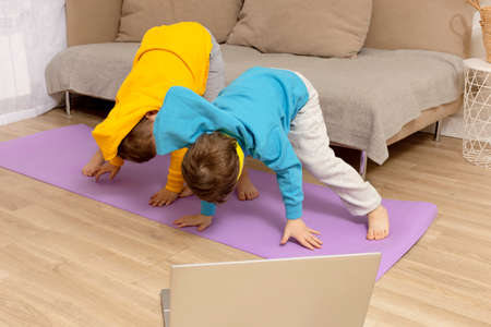 Two little caucasian kids doing fitness exercises at home. Children have fun during sport. Boys make...
