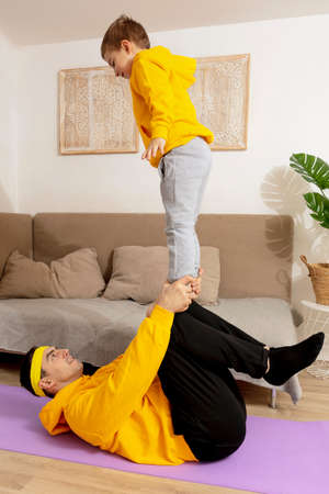Young man with little boy doing fitness exercises at home. Father and son having fun during sport....