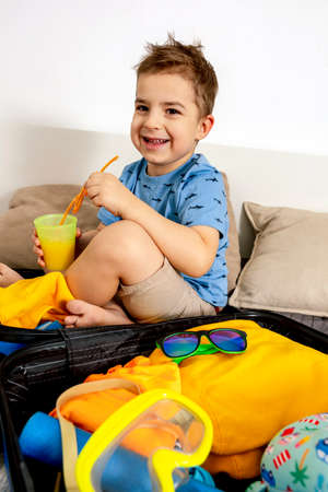 Little caucasian boy with blue shirt ready for vacation. Happy child packs clothes into a suitcase...
