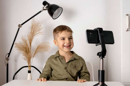 Adorable, cute, little boy blogger recording lifestyle blog, talking to camera of smartphone on tripod. Young influencer filming vlog for his channel. Child makes video for his followers online.の写真素材