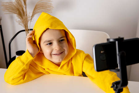 Adorable, cute, little boy blogger recording lifestyle blog, talking to camera of smartphone on...