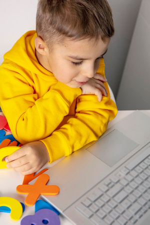 Adorable, cute, little boy learning alphabet online, with laptop at home. Child using e-learning...