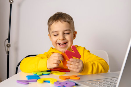 Adorable, cute, little boy learning alphabet online, with laptop at home. Child using e-learning...
