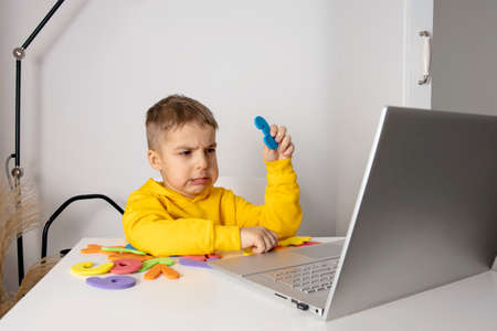 Little boy learning alphabet and numbers online, with laptop at home. Child is sad and tired....