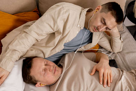 Happy gay couple with casual clothes spending time together at home and listening music with...