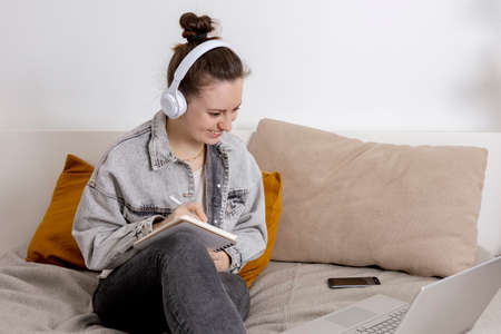 Young beautiful woman with casual clothes sitting on the bed at home with laptop computer and...