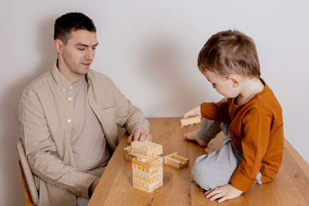 Father and son sitting together at home and playing with wooden blocks. Jenga game. Little boy and his father spending time together. Family time. Leisure activity indoors.の写真素材