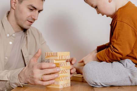 Father and son sitting together at home and playing with wooden blocks. Jenga game. Little boy and his father spending time together. Family time. Leisure activity indoors.の写真素材