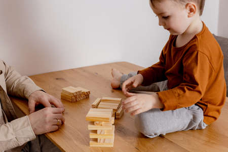 Father and son sitting together at home and playing with wooden blocks. Jenga game. Little boy and his father spending time together. Family time. Leisure activity indoors.の写真素材