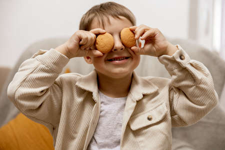 Portrait of little adorable boy holding two biscuits. Kid with cookies. Child and gluten. Healthcare, gluten intolerance by kids. Preschool child with casual clothing. Smile, positive emotions.の写真素材
