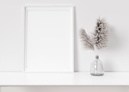 Empty vertical picture frame standing on white shelf. Frame mock up. Copy space for picture, poster. Template for your artwork. Close up view. Pampas grass in vase. 3D rendering.の写真素材