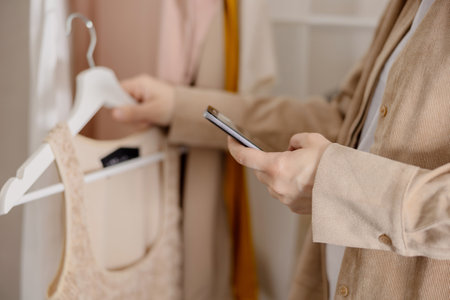 Woman holding smartphone and taking photo of her old clothes to sell them online. Selling on website, e-commerce. Reuse, second-hand concept. Conscious consumer, sustainable lifestyle. Close-up view.の写真素材