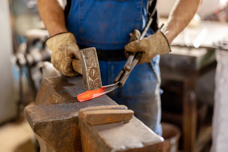 Close up view of heated metal and anvil. The blacksmith in the production process of metal products handmade in the forge. Blacksmith forging metal with a hammer. Metal industry, old profession.の写真素材