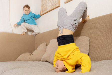 Two active, little kids doing gymnastic handstand exercise in living room. Child standing on hands upside down. Brothers relationship. Children spending time together, having fun during sport.の写真素材