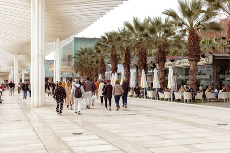 Malaga, Spain- 26-01-2024: Busy promenade in Malaga with people walking and outdoor cafes under a modern canopy, ideal for travel and lifestyle themes. Winter in Spain. Muelle Uno Street.のeditorial素材