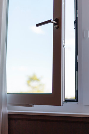 A window is open, allowing sunlight to stream into the room while providing a clear view of trees outside. The fresh air fills the space, enhancing the atmosphereの写真素材