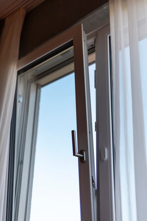 A white framed window is open, allowing sunlight to illuminate the room. Sheer curtains flutter...