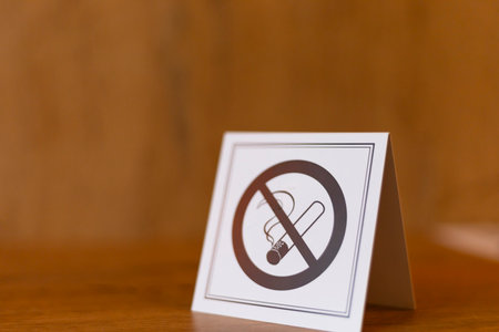 A sign indicating the prohibition of smoking is placed prominently on a wooden table. The bold graphics clearly convey the message to maintain a smoke-free atmosphere in the areaの写真素材