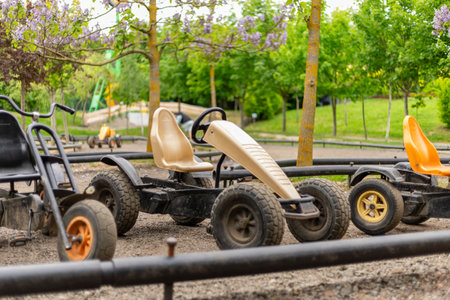 Colorful go-karts sit idle in a well-maintained park, surrounded by lush greenery. Play equipment and pathways are visible, indicating family-friendly recreational spaceの写真素材