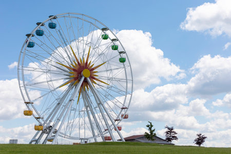 Brightly colored Ferris wheel towers above lush green grass under a sunlit sky, creating a joyful setting at a local fairground on a clear day in summerの写真素材