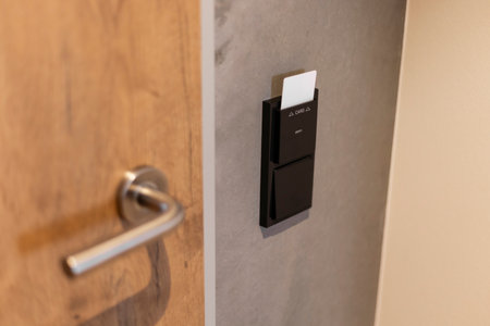 A sleek card reader is installed on a gray wall next to a wooden door. This device allows access using a keycard in a contemporary environment, enhancing security and convenienceの写真素材