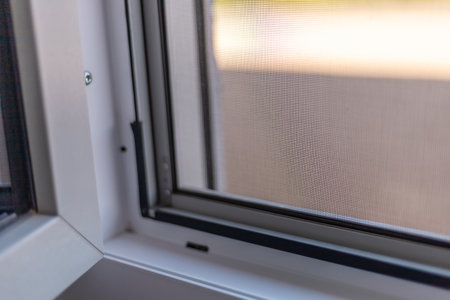 Detailed view of a window frame featuring a mesh screen that offers fly protection. Sunlight filters through, creating a warm and inviting atmosphere as installation is in progressの写真素材