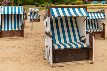 Blue and white striped beach chairs are arranged neatly on the sandy shore, creating a relaxing spot for visitors. The sun shines brightly, inviting leisure and enjoyment in this serene environmentの写真素材