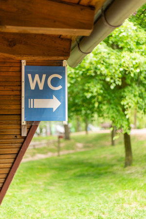 A sign indicating the location of the restroom is attached to a wooden structure, showing a clear arrow pointing to the right amidst lush greenery and trees in daylightの写真素材