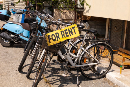 Several bicycles are parked with a prominent sign indicating they are for rent. The scene captures a vibrant outdoor environment with sunny weather and parked motorbikes nearbyの写真素材