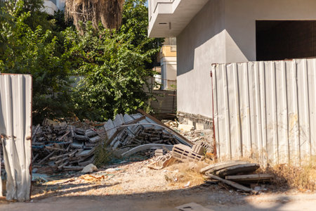 An abandoned construction site showcases scattered debris and overgrown vegetation in a sunny...