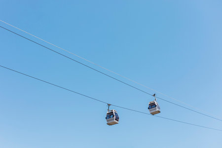 Two cable cars traverse the sky on a cable, showcasing a clear blue background. It is a bright day...