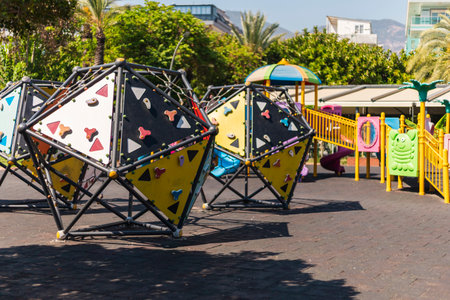 Brightly designed playground features climbing structures set amidst lush greenery and palm trees,...