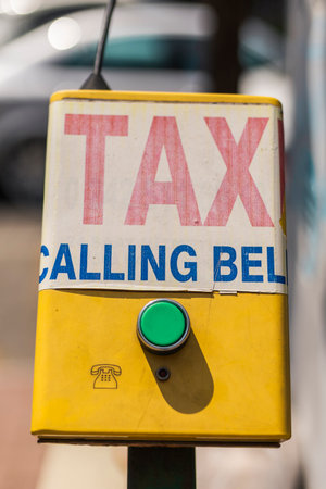 A taxi calling bell is mounted on a pole, prominently displaying its purpose in bold letters. Bright...