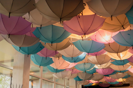 A vibrant array of umbrellas hangs from the ceiling, featuring shades of blue, pink, and white. The unique installation enhances the ambiance of the indoor area, attracting visitorsの写真素材