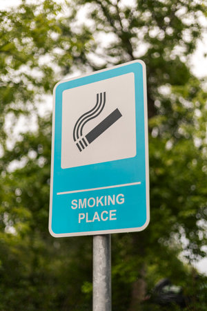 The sign shows a clear symbol and text indicating a smoking place, positioned among lush trees on a...
