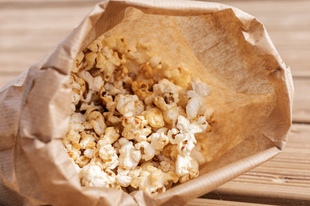 A bag of warm, fluffy popcorn sits on a rustic wooden table, inviting movie lovers to enjoy a tasty snack. Perfect for gatherings or quiet evenings at homeの写真素材