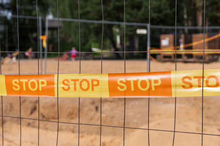 Bright orange stop tape marks off a sand area at a playground, warning visitors of ongoing construction and ensuring safety for childrenの写真素材