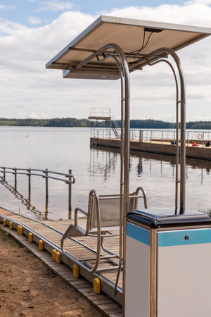 A special sliding chair is positioned on a wooden ramp leading to the lake, providing essential access for disabled individualsの写真素材