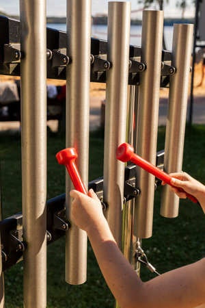 Children are actively engaging with vibrant metal tubes at a park, using red mallets to create...