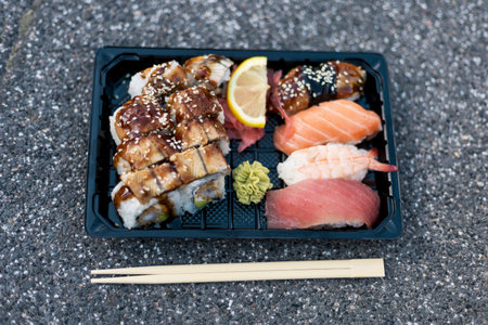 A beautifully arranged platter of sushi includes eel, salmon, and tuna pieces along with fresh ginger, wasabi, and a lemon slice, set on a textured surfaceの写真素材