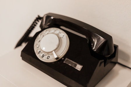 A classic rotary telephone sits on a smooth white surface, showcasing its elegant black design. This...