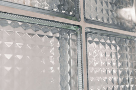 Close-up view of clear glass blocks with varied textures allowing light to pass through. The design...